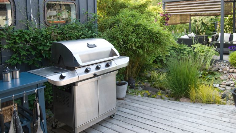 Ein gro&szlig;er Gasgrill steht auf einer h&ouml;lzernen Terrasse. Daneben befindet sich ein Arbeitsbereich mit K&uuml;chenutensilien.