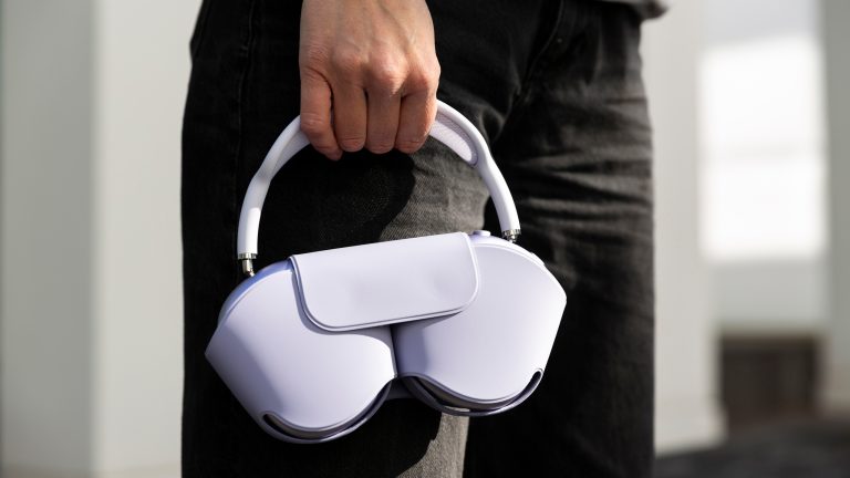 Eine Person h&auml;lt die AirPods Max 2 in Violett am Kopfband fest, w&auml;hrend sie im Smart Case verstaut sind.