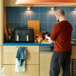 Eine Person bereitet frisches Gem&uuml;se und Obst auf einer K&uuml;chenarbeitsplatte vor, im Hintergrund eine Hei&szlig;luftfritteuse.