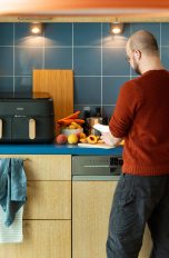 Heißluftfritteuse richtig nutzen - Tipps für perfekte Ergebnisse Eine Person bereitet frisches Gemüse und Obst auf einer Küchenarbeitsplatte vor, im Hintergrund eine Heißluftfritteuse.