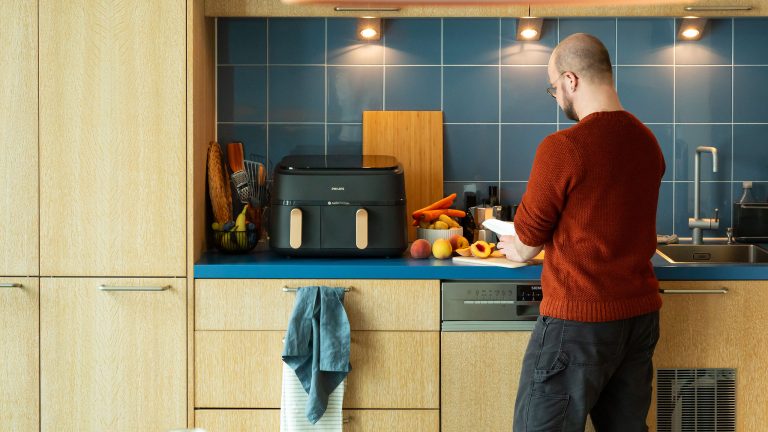 Eine Person bereitet frisches Gem&uuml;se und Obst auf einer K&uuml;chenarbeitsplatte vor, im Hintergrund eine Hei&szlig;luftfritteuse.