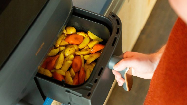 Heißluftfritteuse richtig nutzen - Tipps für perfekte Ergebnisse Ein geöffneter Garkorb einer Heißluftfritteuse mit gewürzten Kartoffelspalten und Karottenstücken, von oben fotografiert.