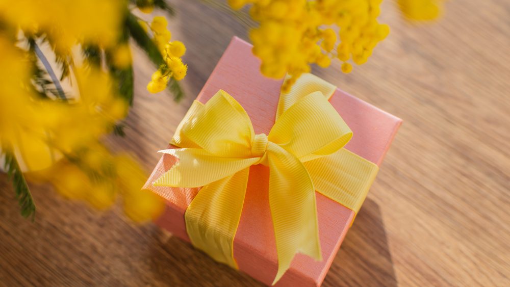 Bild von einem kleinen Geschenk, das unterhalb eines Blumenstrau&szlig;es liegt.