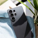 Detailaufnahme der R&uuml;ckseite des Samsung Galaxy S26 Ultra, das auf einer hellblauen Unterlage auf einem Holzschreibtisch liegt.