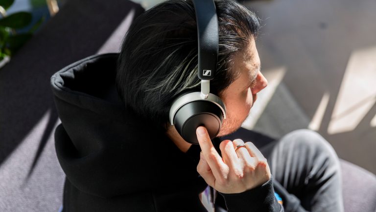 Eine Person sitzt auf einem Sessel und bedient die Touch-Schaltfl&auml;che an der rechten Ohrmuschel der Sennheiser HDB 630.