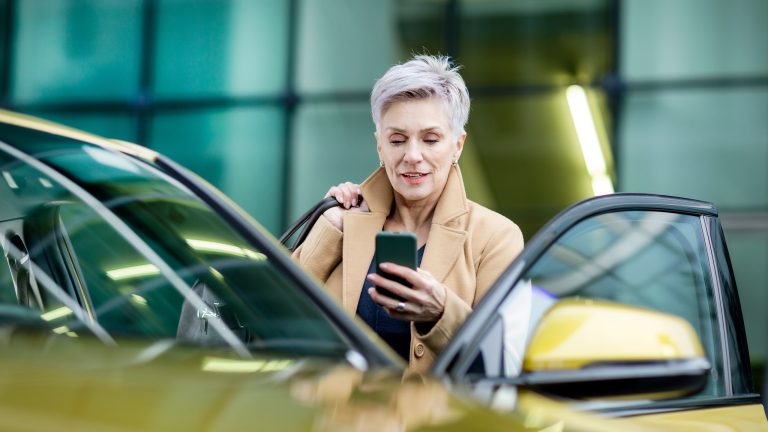 Eine Person mit einem Handy in der Hand steht in der ge&ouml;ffneten T&uuml;r eines Autos.
