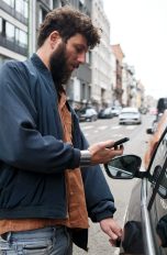 Carsharing-Apps, Ohne eigenes Auto fahren Eine Person steht neben einem Auto und scheint dieses über ihr Handy zu entsperren.