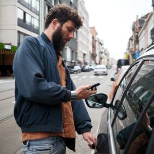 Eine Person steht neben einem Auto und scheint dieses &uuml;ber ihr Handy zu entsperren.