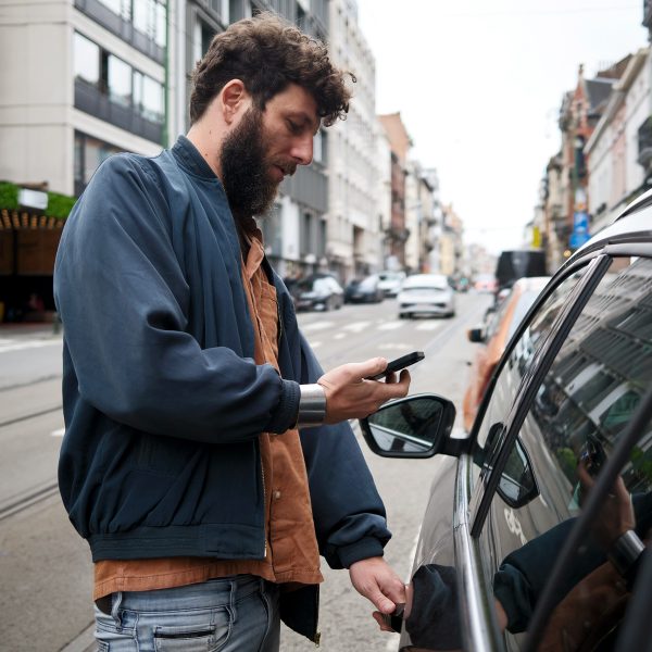 Eine Person steht neben einem Auto und scheint dieses &uuml;ber ihr Handy zu entsperren.