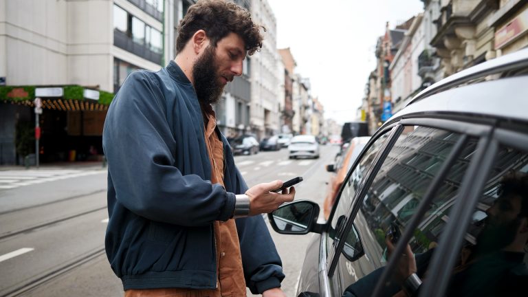 Eine Person steht neben einem Auto und scheint dieses &uuml;ber ihr Handy zu entsperren.