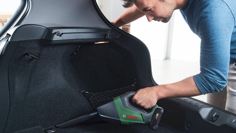 Eine Person h&auml;lt einen Bosch UniversalVac 18 in der Hand und saugt damit den Kofferraum eines Autos aus.