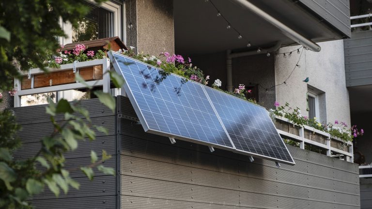 An einem Balkon in einem Mehrfamilienhaus ist ein Balkonkraftwerk montiert.