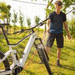 Eine Person steht auf einem Rasen und w&auml;scht ihr wei&szlig;es E-Mountainbike mit einem Gartenschlauch ab.