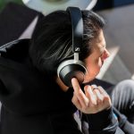 Eine Person sitzt auf einem Sofa und tr&auml;gt Sennheiser HDB 630. Sie tippt mit ihrerm rechten Zeigefinger auf das Touch-Bedienfeld der rechten Ohrmuschel.