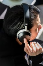 Kopfhörer, Welche Arten es gibt und wann sie glänzen Eine Person sitzt auf einem Sofa und trägt Sennheiser HDB 630. Sie tippt mit ihrerm rechten Zeigefinger auf das Touch-Bedienfeld der rechten Ohrmuschel.