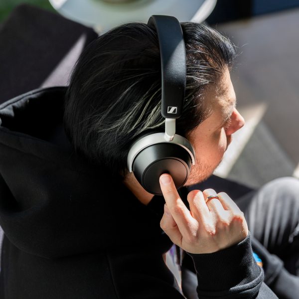 Eine Person sitzt auf einem Sofa und tr&auml;gt Sennheiser HDB 630. Sie tippt mit ihrerm rechten Zeigefinger auf das Touch-Bedienfeld der rechten Ohrmuschel.