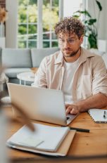 Lebenslauf in Word erstellen, So funktioniert es Eine Person sitzt an einem Tisch mit einem Laptop vor sich und scheint etwas zu tippen. Vor dem Laptop liegen einige Dokumente.