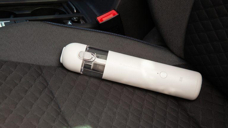 Der Xiaomi Mi Vacuum Cleaner Mini liegt auf einem Autositz mit Stoff-Bezug.
