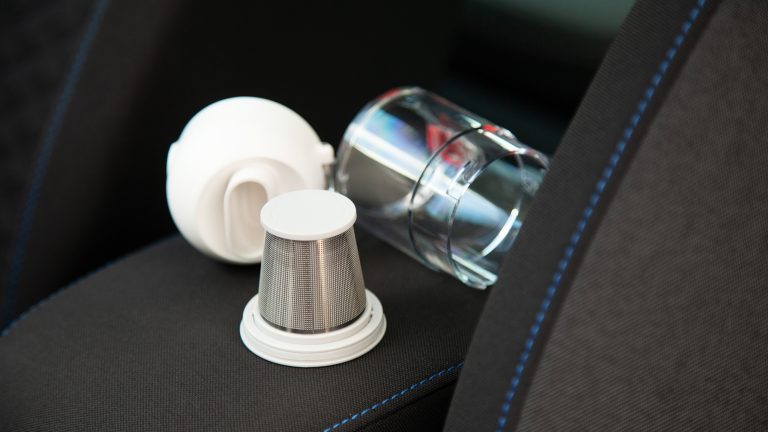 D&uuml;se, Filter und Auffangbeh&auml;lter des Xiaomi Mi Vacuum Cleaner Mini liegen ausgebaut auf der Armlehne eines Autos.
