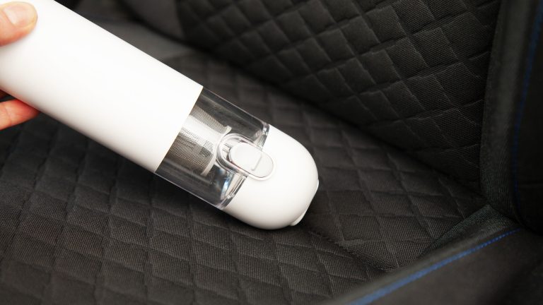 Eine Person saugt mit dem Xiaomi Mi Vacuum Cleaner Mini in die Ritze bei einem Autositz.