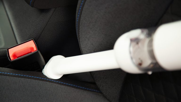 Eine Person saugt mit dem Xiaomi Mi Vacuum Cleaner Mini mit aufgesteckter B&uuml;rstend&uuml;se entlang des Gurtverschlusses im Auto.