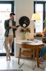 Smart Home in der Mietwohnung, Das solltest du wissen Zwei Personen befinden sich in einer Wohnung. Eine Person sitzt an einem Tisch und begutachtet eine Lampe, die über ihrem Kopf hängt. Die zweite Person bedient diese mit einem Tablet.