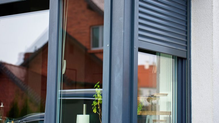 Bild von halb geschlossenen Rolll&auml;den an einem Eckfenster eines Hauses.