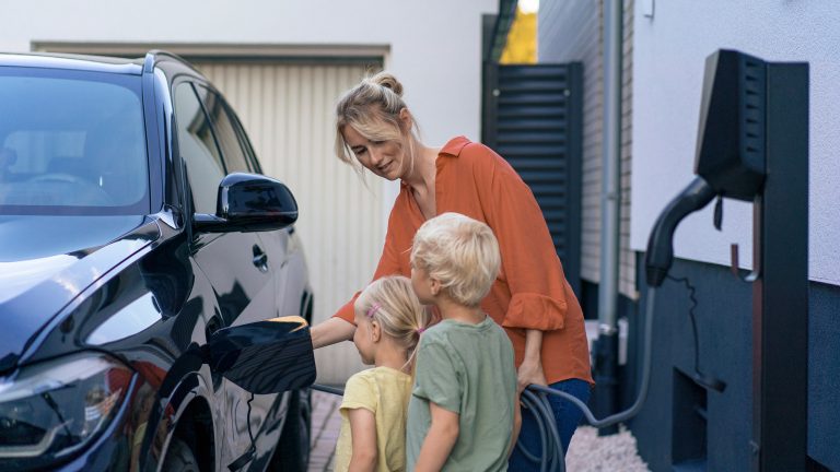 Eine Person schlie&szlig;t ein Elektroauto an eine Wallbox an, w&auml;hrend ihre Kinder dabei zusehen.