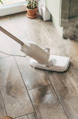 Dampfreiniger, Tipps und Tricks für die gründliche Reinigung Eine Person reinigt einen Holzboden mit einem Dampfreiniger, während Dampf aus dem Gerät aufsteigt.
