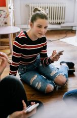 So machst du dein Device kindersicher Drei junge Personen sitzen auf dem Boden in einem Zimmer. Alle drei halten ein Smartphone in der Hand.