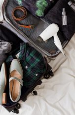 Unterwegs die Haare trocknen, 5 kompakte Reiseföhn-Modelle (Ein Bild von einem Reiseföhn, der zusammen mit Schuhen, einem Gürtel, einer Schlafmaske und mehr in einem geöffneten Koffer auf einem Bett liegt.)