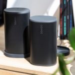 Zwei schwarze Sonos Play stehen nebeneinander auf einem Schreibtisch. Ein Lautsprecher steht in der Ladestation, der andere frei.