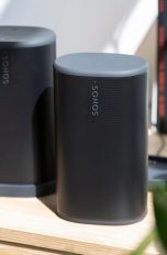 Zwei schwarze Sonos Play stehen nebeneinander auf einem Schreibtisch. Ein Lautsprecher steht in der Ladestation, der andere frei.
