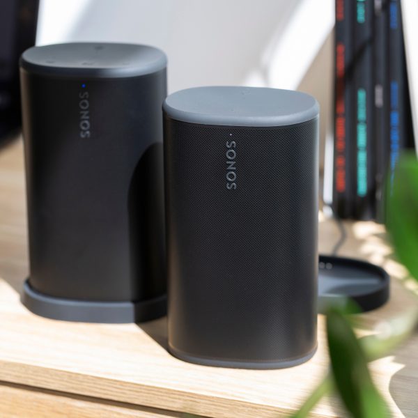 Zwei schwarze Sonos Play stehen nebeneinander auf einem Schreibtisch. Ein Lautsprecher steht in der Ladestation, der andere frei.