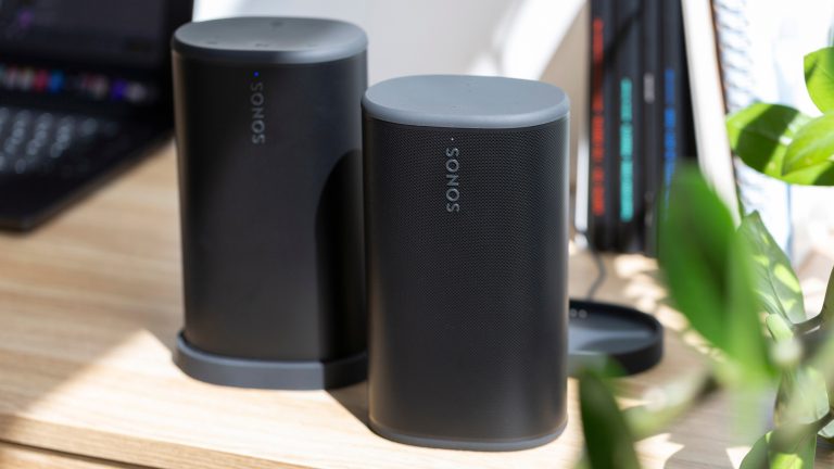 Zwei schwarze Sonos Play stehen nebeneinander auf einem Schreibtisch. Ein Lautsprecher steht in der Ladestation, der andere frei.