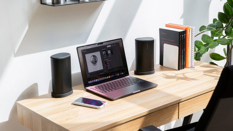Ein Arbeitsplatz mit einem MacBook Pro, einem iPhone und zwei Sonos Play links und rechts vom Laptop.