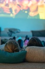 Beamer defekt, Die typischen Probleme und Lösungen Fünf Personen liegen auf einem Sofa und schauen in Richtung eines Beamer-Bildes an die Wand.