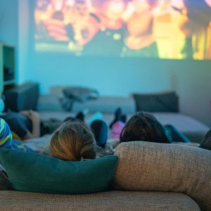 F&uuml;nf Personen liegen auf einem Sofa und schauen in Richtung eines Beamer-Bildes an die Wand.
