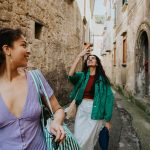 Zwei Personen befinden sich in einer engen steinernen Gasse. Eine Person nimmt ein Foto mit ihrem Smartphone auf, die andere blickt dabei &uuml;ber ihre Schulter.