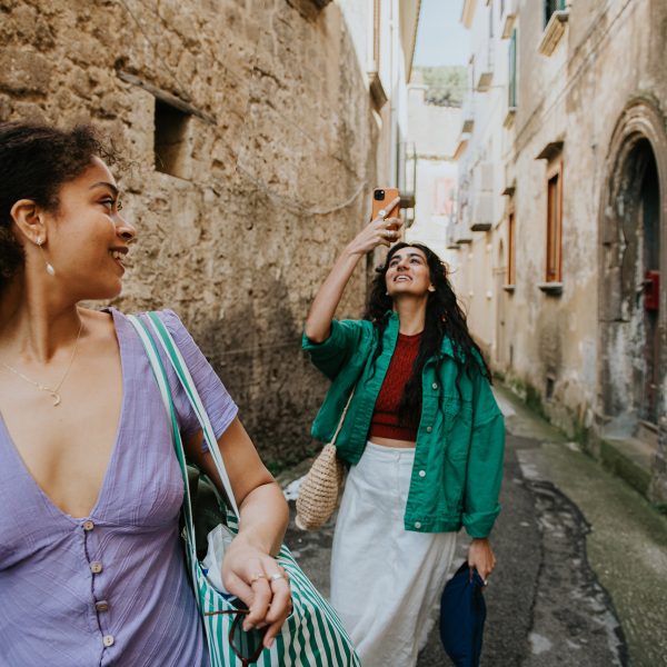 Zwei Personen befinden sich in einer engen steinernen Gasse. Eine Person nimmt ein Foto mit ihrem Smartphone auf, die andere blickt dabei &uuml;ber ihre Schulter.