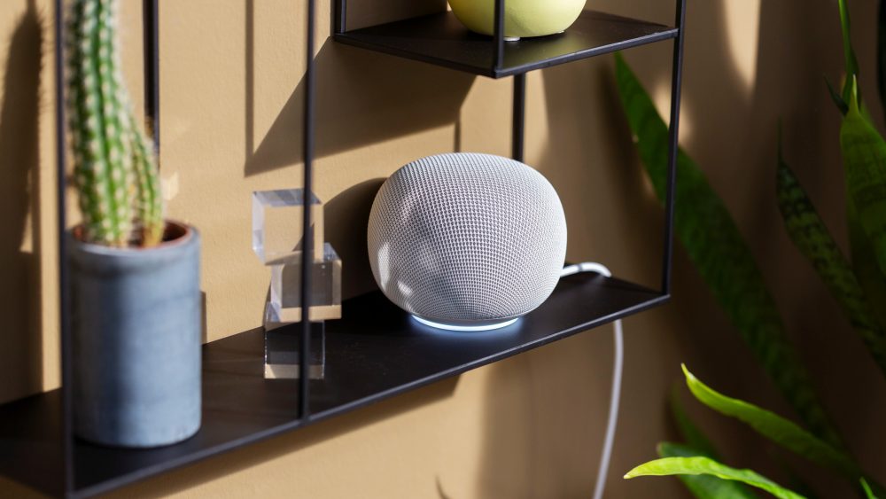 Ein Google Home Speaker in Wei&szlig; steht auf einem schwarzen Regal.