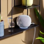Ein Google Home Speaker in Wei&szlig; steht auf einem schwarzen Regal.