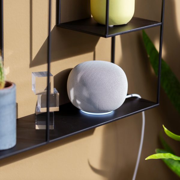 Ein Google Home Speaker in Wei&szlig; steht auf einem schwarzen Regal.