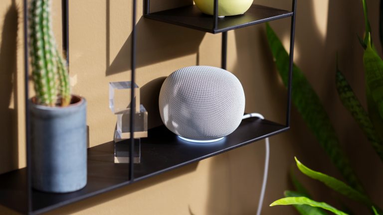 Ein Google Home Speaker in Wei&szlig; steht auf einem schwarzen Regal.