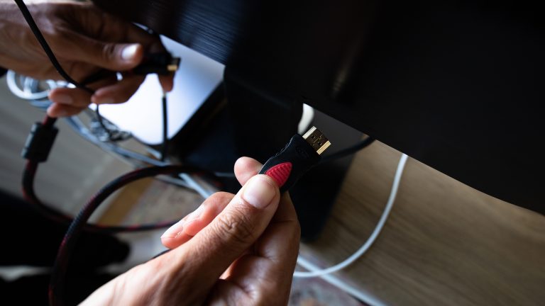 HDMI 2.1 vs. eARC, Was du wirklich brauchst Eine Person schließt auf der Rückseite eines Fernsehers ein HDMI-Kabel an.