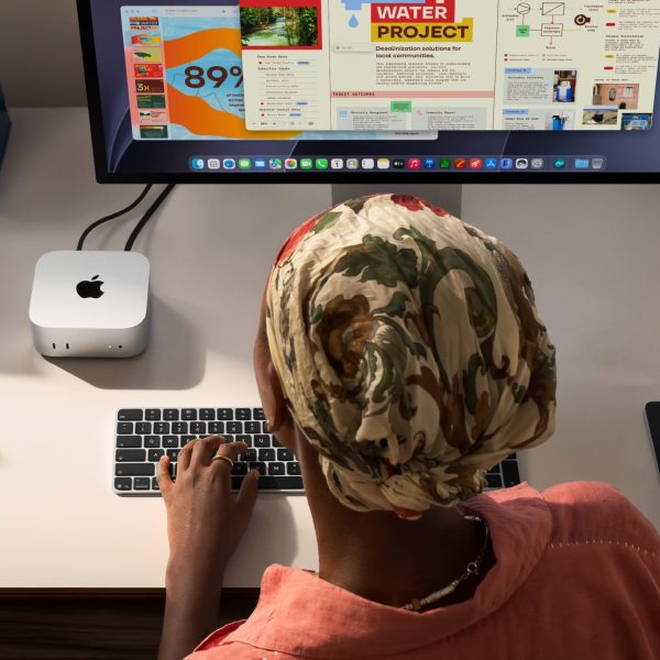 Eine Person sitzt an einem Arbeitsplatz, auf dem links neben dem Monitor ein Mac Mini steht.