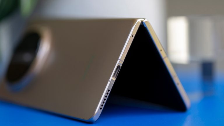 Honor Magic V6, Schicker, schneller, ausdauernder Ein leicht aufgeklapptes Honor Magic V6 steht auf einem blauen Regal.