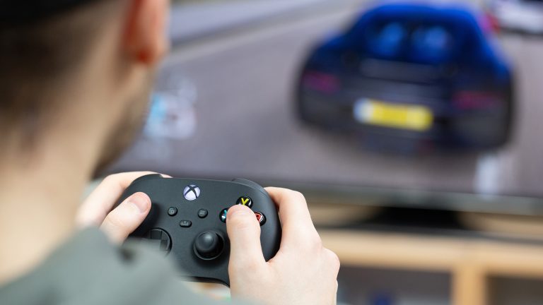 Eine Person sitzt mit einem Controller in der Hand vor einem Fernseher und spielt etwas auf einer Xbox.