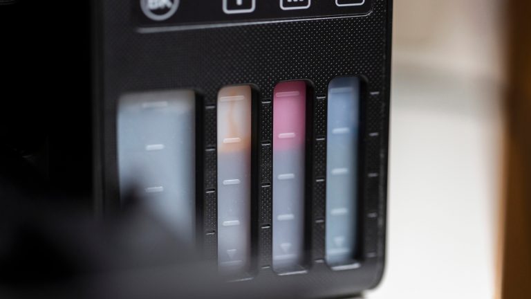 Tintenstrahldrucker, Patrone oder Tank - so triffst du die richtige Wahl Nahaufnahme von vier Tintentanks eines Druckers, jeweils mit farbiger Tinte und Füllstandsanzeige für Schwarz, Gelb, Magenta und Cyan.