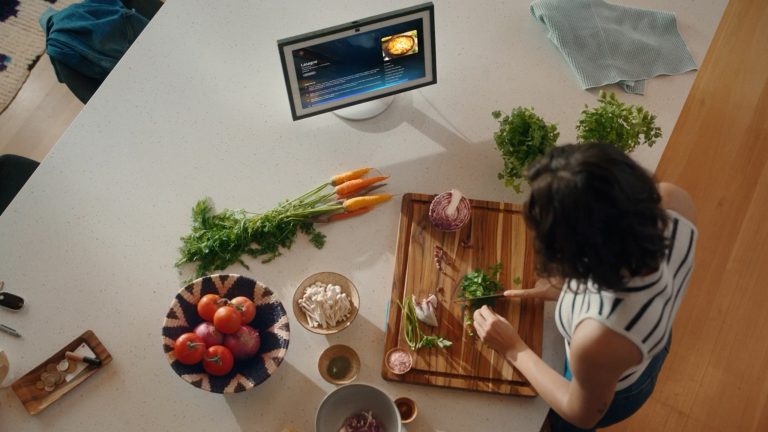 Eine Person steht in der K&uuml;che und schneidet etwas Gem&uuml;se. Auf der K&uuml;chenzeile steht ein Echo Show mit Alexa+.